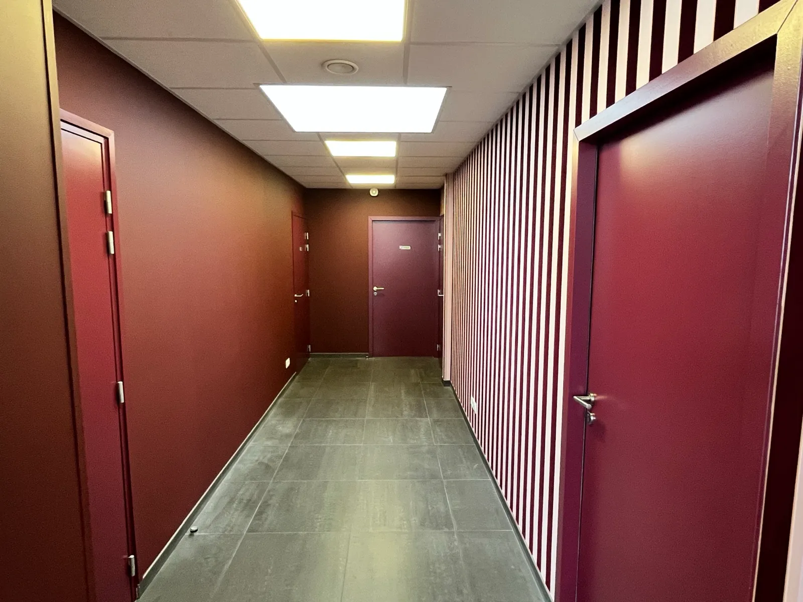 Couloir de bureaux aux murs bordeaux et mur rayé
