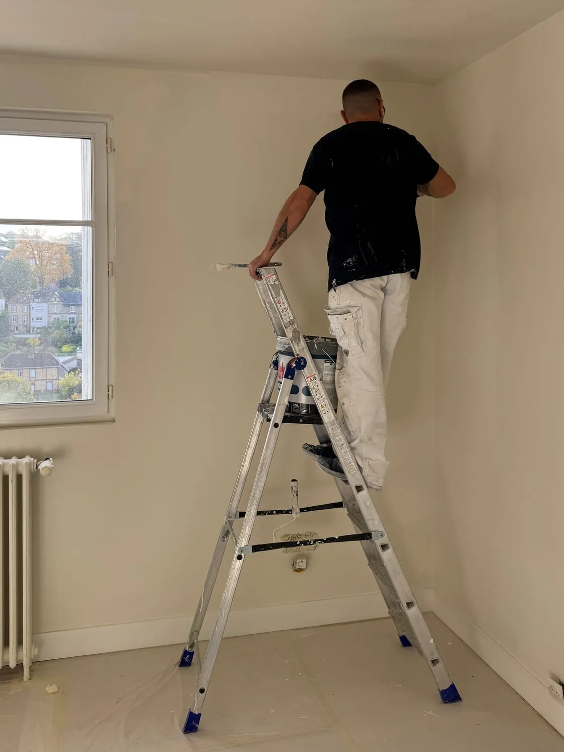 Un peintre de Fresnel sur un escabeau, en train de peindre le haut d’un mur